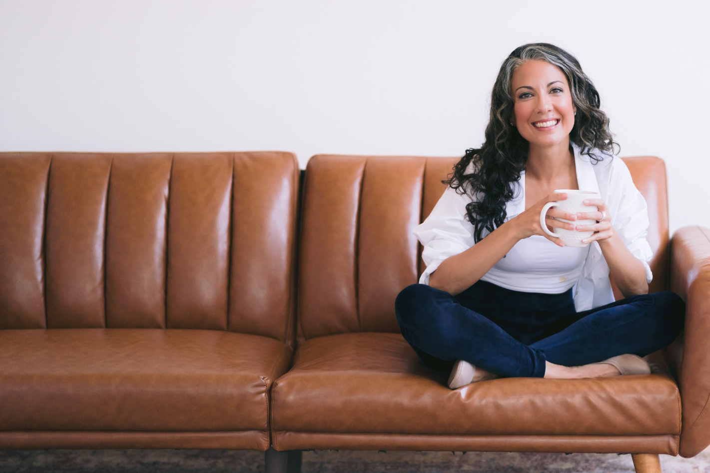 Coach smiling while sitting cross-legged on a couch holding a mug